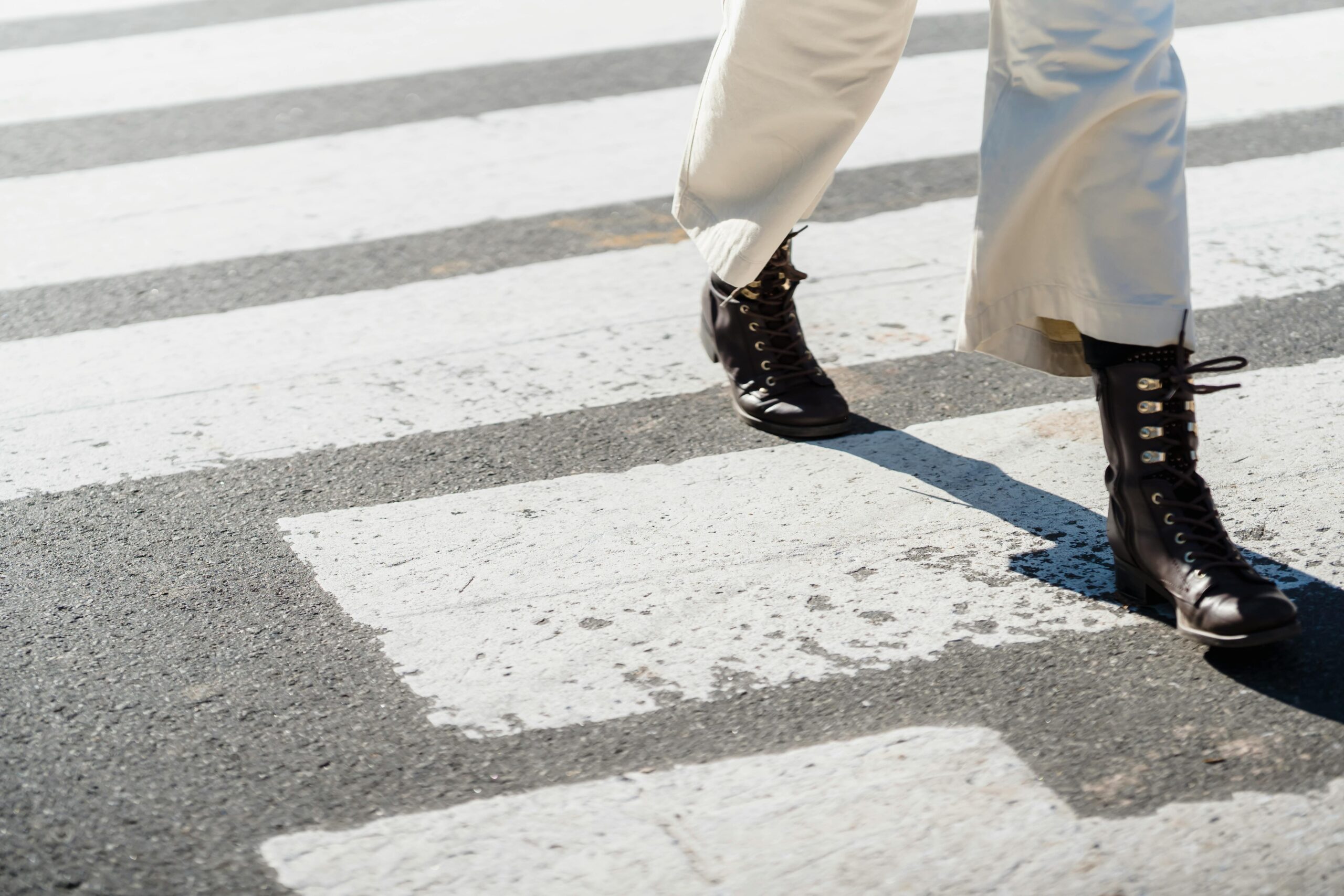 A woman in stylish boots walks across a city crosswalk capturing urban fashion and movement.